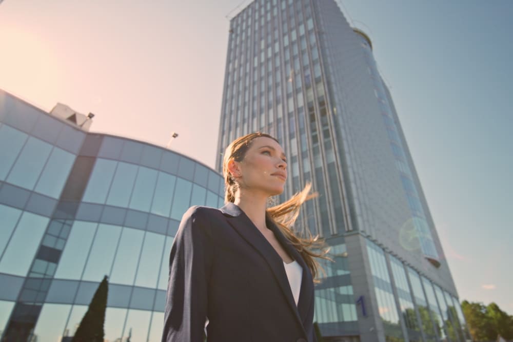 Уверенная деловая женщина на фоне современного небоскрёба с зеркальным фасадом под солнечным светом
