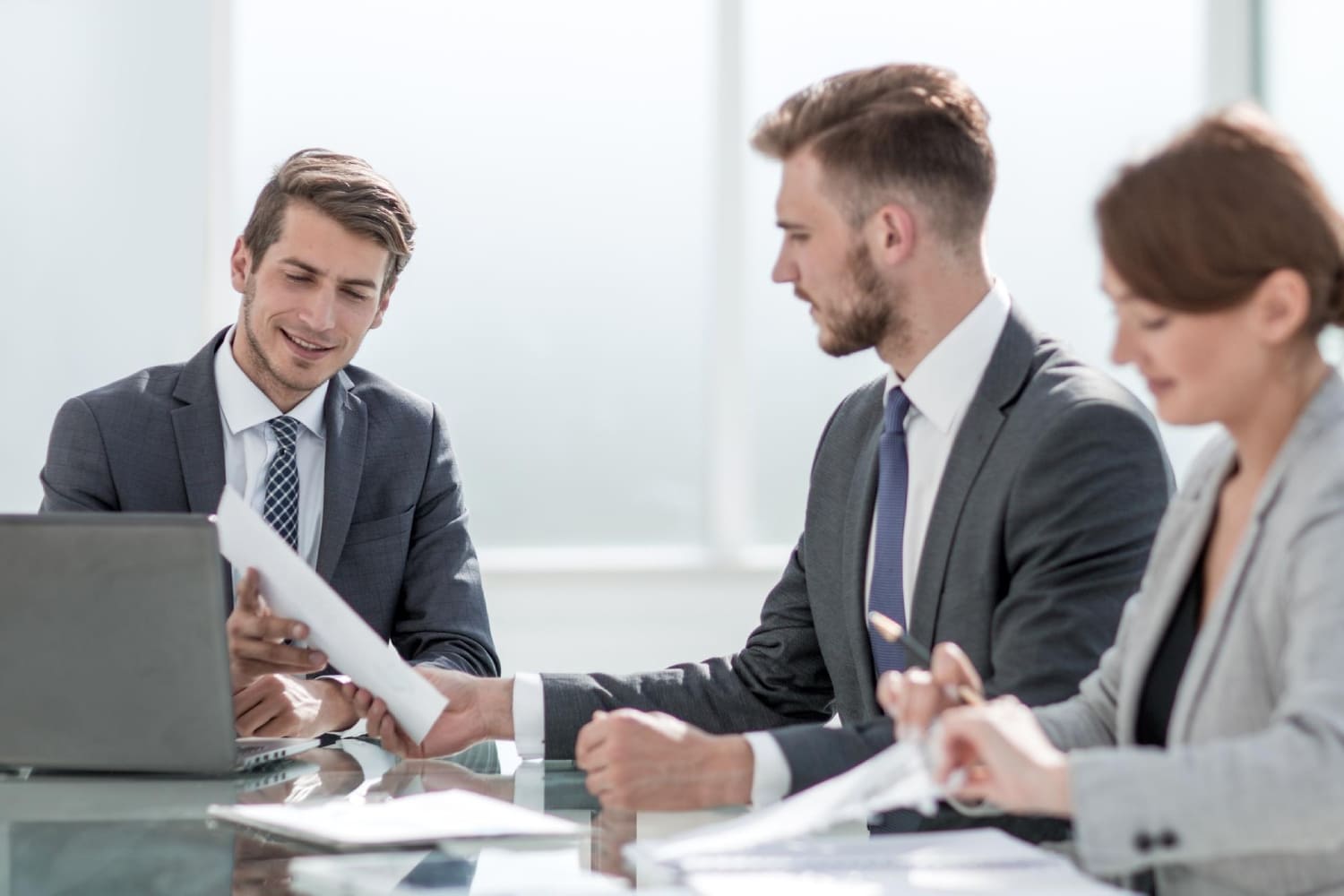 Трое специалистов в деловой одежде обсуждают финансовые документы за офисным столом