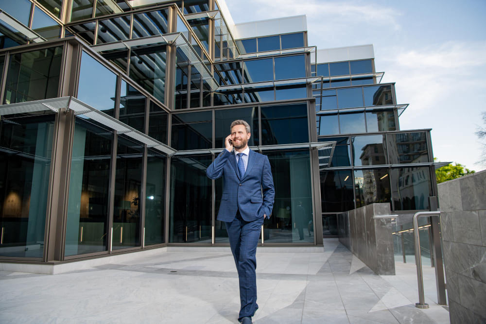 Деловой мужчина в костюме выходит из современного здания и говорит по телефону