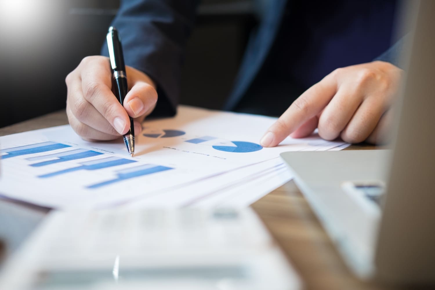Рука с ручкой указывает на графики роста на инвестиционном отчёте