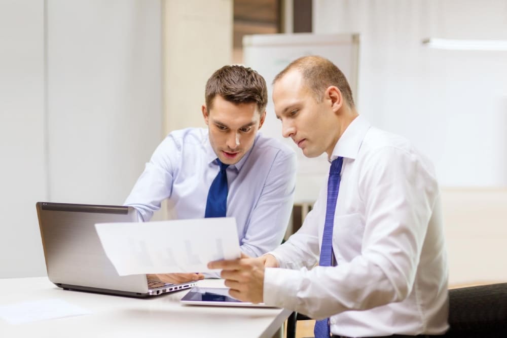 Два деловых мужчины обсуждают документы с финансовыми графиками за ноутбуком