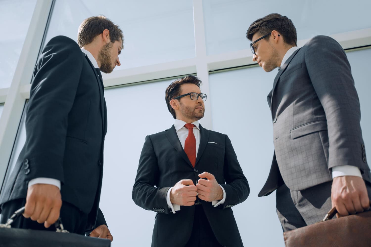 Трое мужчин в деловых костюмах обсуждают сделку, стоя в офисном здании